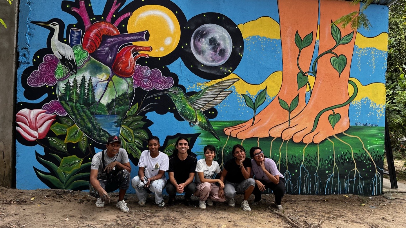 Equipo de la colectiva frente a un mural comunitario pintado por ellos